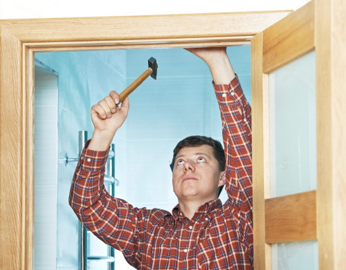 Male handyman carpenter at interior wood door installation with hammer